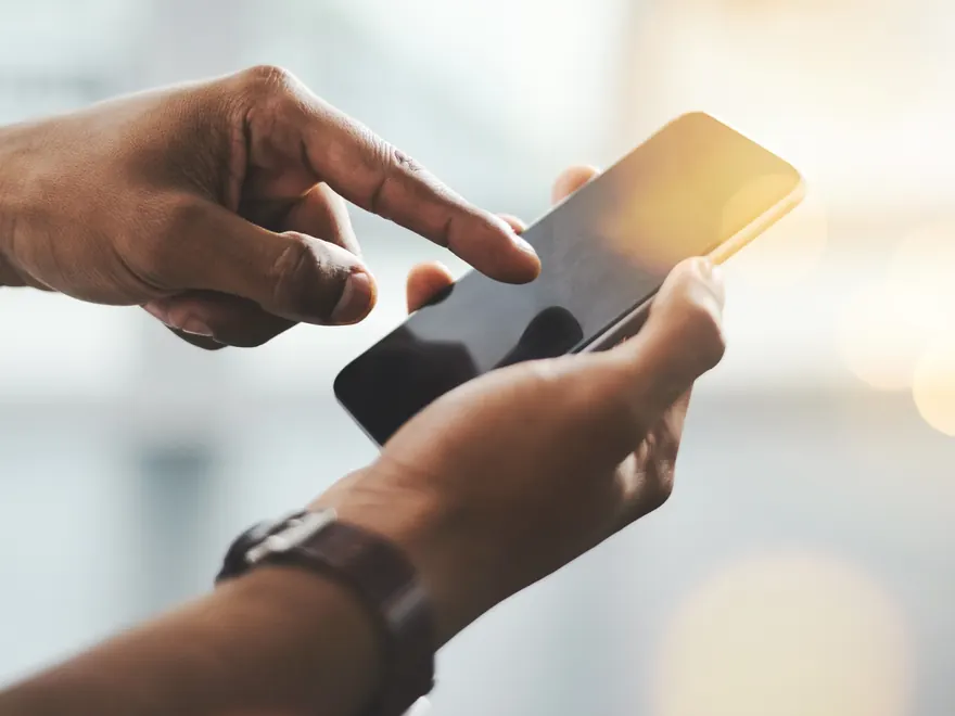 Två händer som håller i och pekar på en mobiltelefon